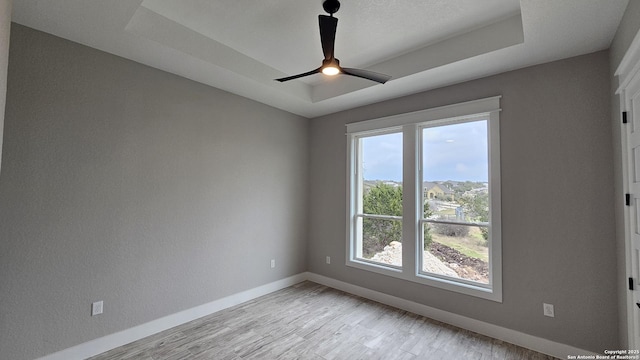 spare room featuring ceiling fan, light wood-style flooring, baseboards, and a raised ceiling