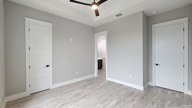 unfurnished bedroom with a tray ceiling, light wood-style flooring, visible vents, and baseboards