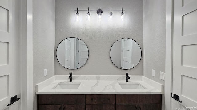 full bathroom with a textured wall, a sink, and double vanity