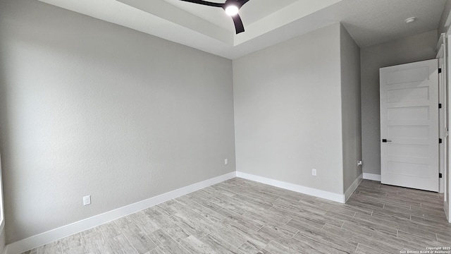 spare room with light wood-style floors, a raised ceiling, baseboards, and a ceiling fan