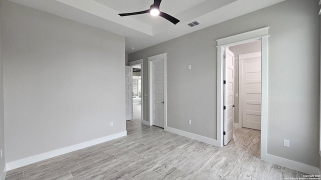 unfurnished bedroom with light wood-style floors, a tray ceiling, and baseboards