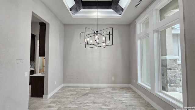 unfurnished dining area with light wood-style flooring, a tray ceiling, a chandelier, and baseboards