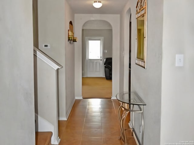 hallway with baseboards, arched walkways, and tile patterned floors