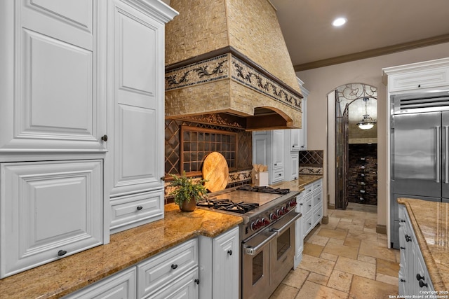 kitchen with stone tile floors, high end appliances, tasteful backsplash, ornamental molding, and white cabinetry