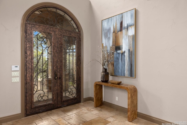 foyer entrance featuring baseboards, french doors, arched walkways, and stone tile floors