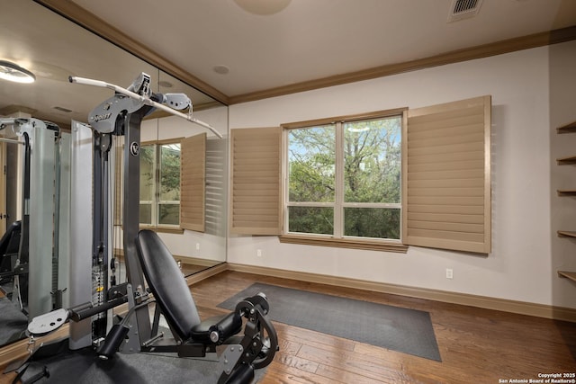 exercise area featuring visible vents, crown molding, baseboards, and wood finished floors