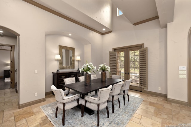 dining area with arched walkways, french doors, stone tile flooring, a towering ceiling, and baseboards