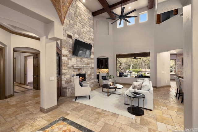 living area featuring a fireplace, stone tile flooring, ceiling fan, beamed ceiling, and baseboards