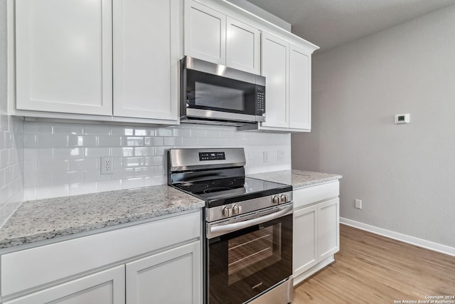 kitchen with baseboards, decorative backsplash, stainless steel appliances, light wood-type flooring, and white cabinetry