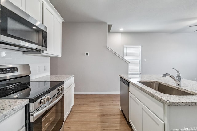 kitchen with a sink, white cabinets, light wood-style floors, appliances with stainless steel finishes, and decorative backsplash