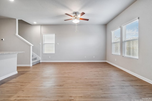 spare room featuring stairs, ceiling fan, light wood-style floors, and baseboards