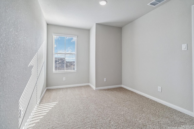 empty room with baseboards, visible vents, and light colored carpet