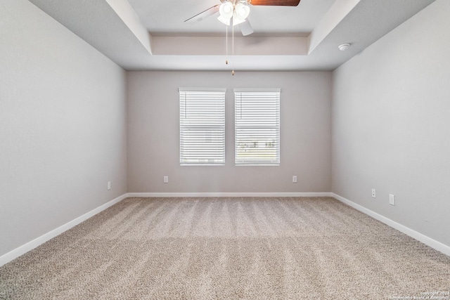 carpeted spare room featuring a raised ceiling, a ceiling fan, and baseboards