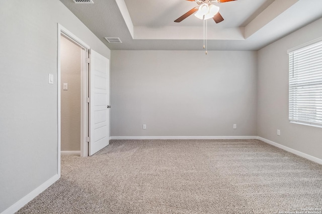 unfurnished room with a raised ceiling, light colored carpet, and baseboards