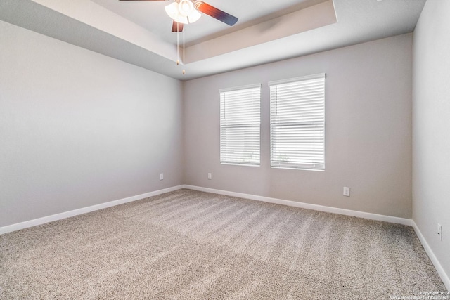 carpeted spare room featuring ceiling fan, a tray ceiling, and baseboards