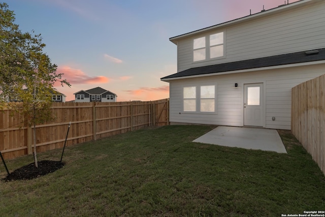 back of house at dusk with a lawn, a patio area, and a fenced backyard