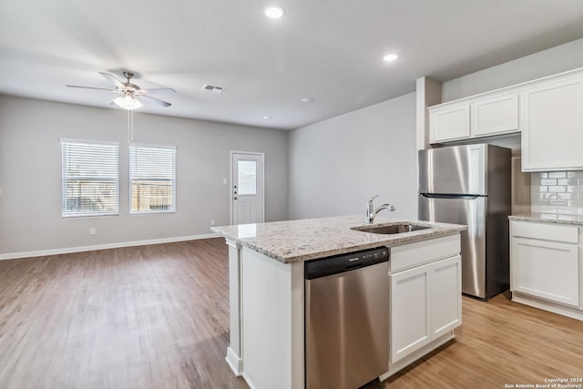 kitchen with light wood finished floors, stainless steel appliances, tasteful backsplash, a kitchen island with sink, and a sink