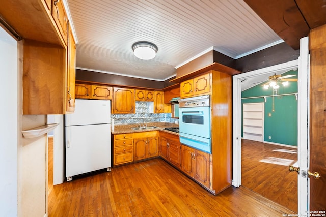 kitchen featuring white appliances, ornamental molding, brown cabinets, a sink, and a warming drawer