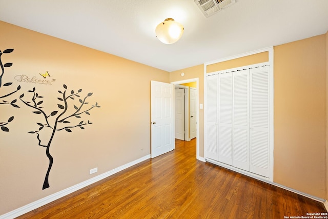 unfurnished bedroom featuring a closet, visible vents, baseboards, and wood finished floors