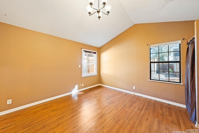 unfurnished room featuring lofted ceiling, a textured ceiling, baseboards, light wood-style floors, and an inviting chandelier