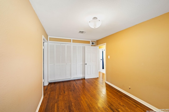 unfurnished bedroom featuring a closet, visible vents, baseboards, and wood finished floors