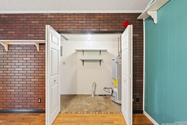 laundry room featuring brick wall, water heater, a textured ceiling, and wood finished floors