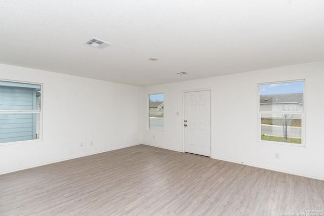 unfurnished room featuring plenty of natural light, visible vents, and light wood-style floors