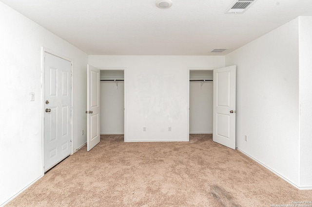 unfurnished bedroom featuring light carpet, a textured ceiling, visible vents, and multiple closets