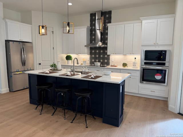 kitchen with light wood-style flooring, light countertops, wall chimney range hood, backsplash, and freestanding refrigerator