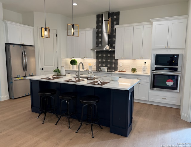 kitchen with light wood finished floors, decorative backsplash, stainless steel appliances, light countertops, and wall chimney range hood