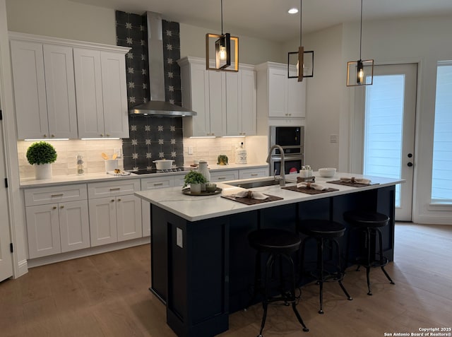 kitchen featuring wall chimney exhaust hood, black electric stovetop, light countertops, and light wood-style floors