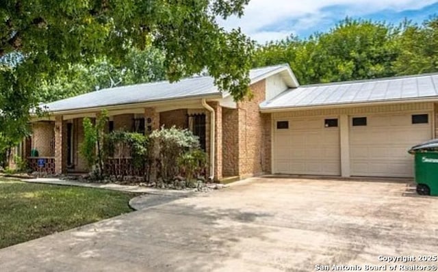 ranch-style house with metal roof, concrete driveway, a standing seam roof, and an attached garage