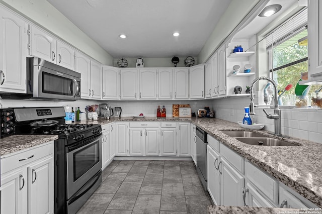 kitchen with white cabinets, light stone counters, stainless steel appliances, and a sink