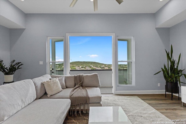 living room featuring ceiling fan, baseboards, and wood finished floors