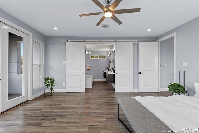 bedroom with wood finished floors, visible vents, baseboards, and a barn door