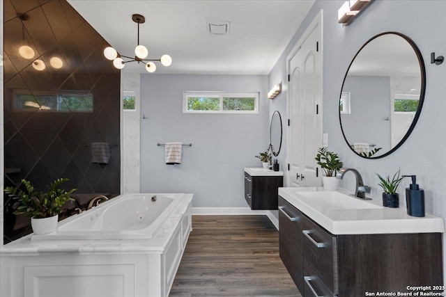 full bath featuring two vanities, a sink, wood finished floors, baseboards, and a tub with jets