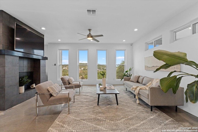 living area with a ceiling fan, visible vents, a tiled fireplace, and recessed lighting