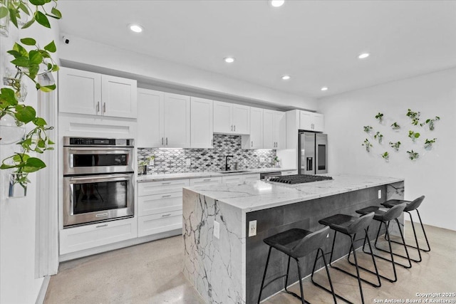 kitchen featuring stainless steel appliances, a sink, white cabinetry, tasteful backsplash, and a kitchen bar