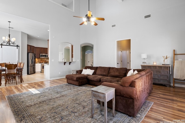 living room featuring light wood-style floors, arched walkways, visible vents, and ceiling fan with notable chandelier