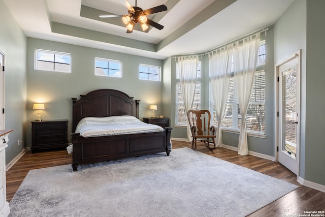 bedroom with wood finished floors, a raised ceiling, a ceiling fan, and baseboards