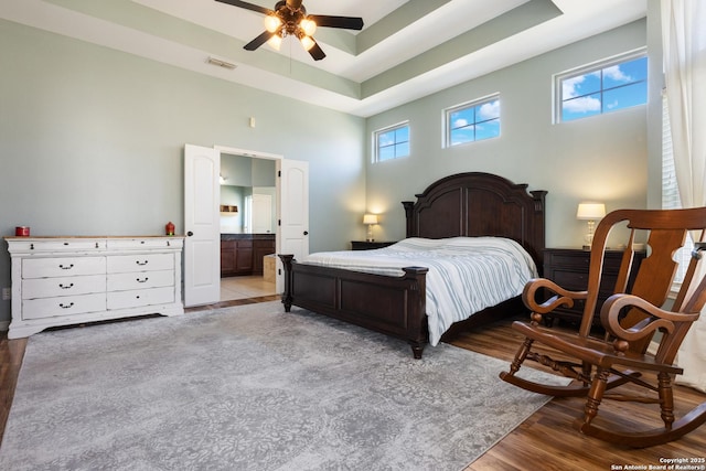 bedroom featuring light wood-style floors, multiple windows, visible vents, and a tray ceiling