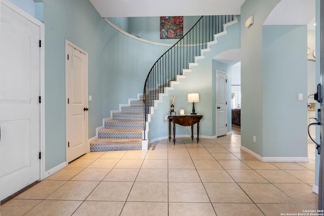 foyer entrance featuring light tile patterned floors, baseboards, a high ceiling, and arched walkways