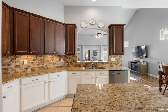 kitchen with arched walkways, decorative backsplash, light stone counters, a sink, and stainless steel dishwasher