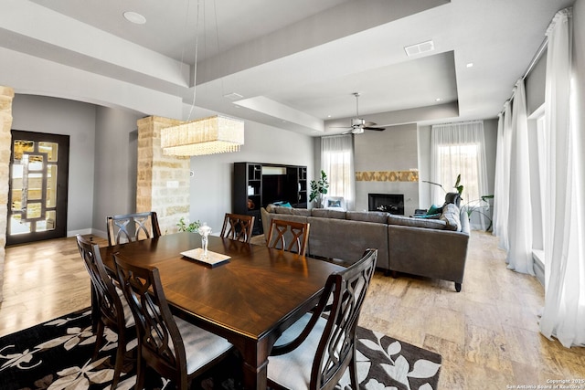 dining room with light wood finished floors, visible vents, a raised ceiling, ceiling fan, and a fireplace