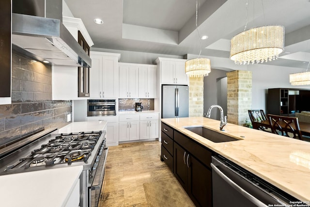 kitchen featuring appliances with stainless steel finishes, white cabinets, a sink, and wall chimney exhaust hood