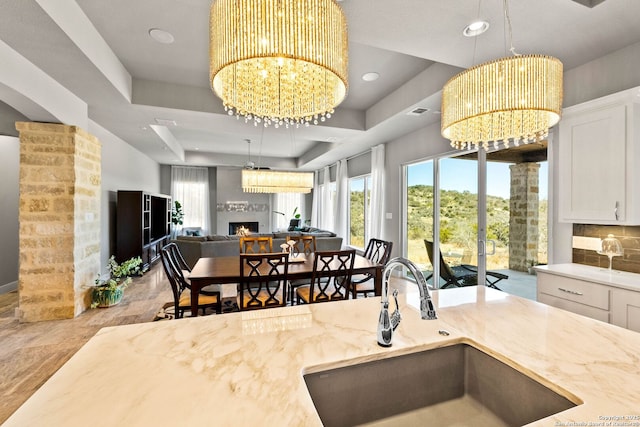 kitchen with light stone countertops, a lit fireplace, a chandelier, and a tray ceiling