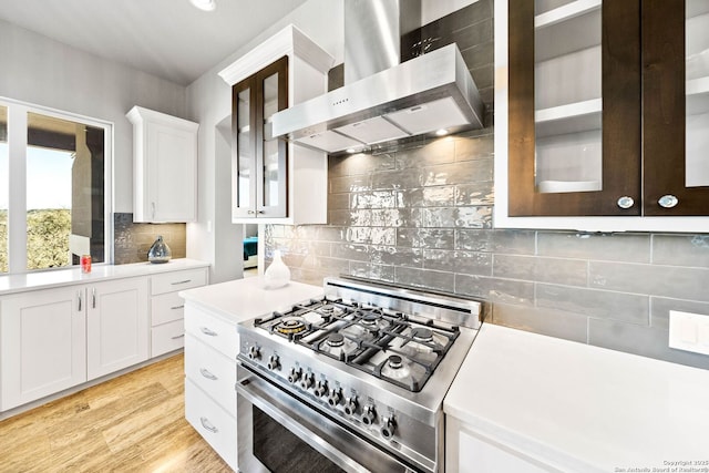 kitchen with white cabinets, light wood-style floors, light countertops, wall chimney range hood, and stainless steel gas stove