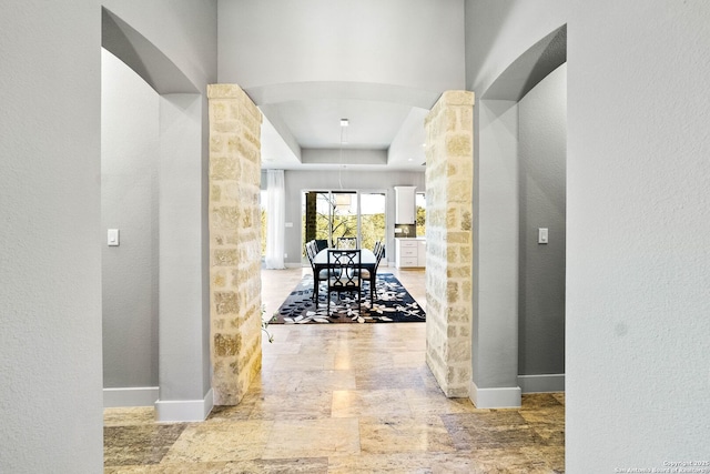 hallway featuring arched walkways, stone finish floor, a tray ceiling, and baseboards