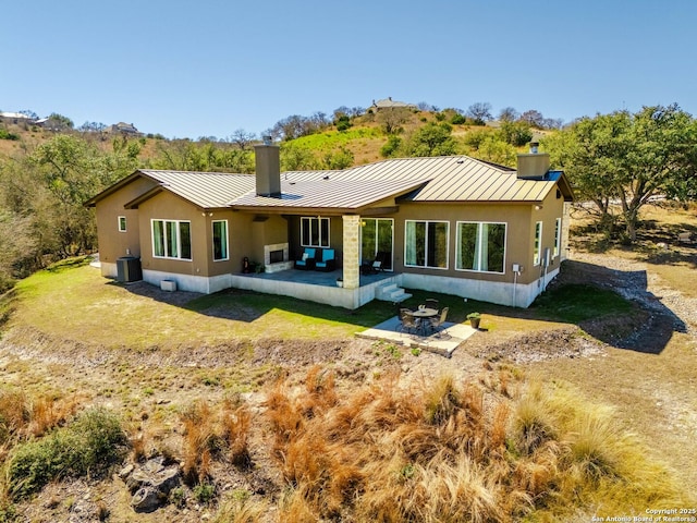 back of property with a standing seam roof, a patio area, a chimney, and metal roof