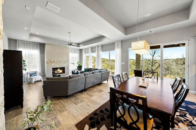 dining room with a large fireplace, wood finished floors, visible vents, a ceiling fan, and a raised ceiling